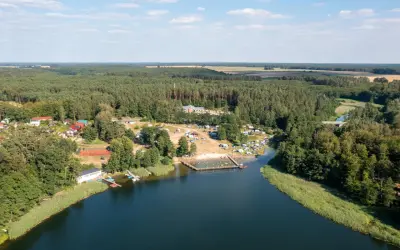 Widok z lotu ptaka na jezioro, plażę z ludźmi, kemping i las. Sprawdź jezioro przechlewskie cennik na wakacje.