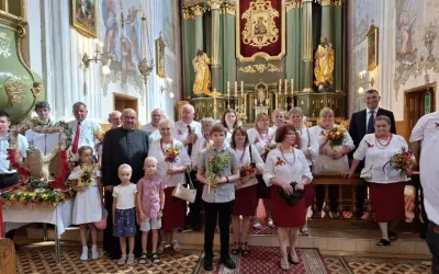 Uroczystość Wniebowzięcia Najświętszej Maryi Panny w kościele. Grupa osób w strojach ludowych i duchowny pozują do zdjęcia.