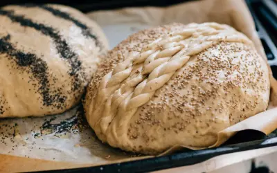Två nybakade bröd på bakplåtspapper, ett toppat med vallmofrön och ett med sesamfrön och flätat mönster. Perfekta fika idéer!