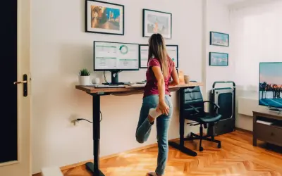 Une femme s'étire près d'un bureau réglable en hauteur, parfait pour faire un bureau avec un plan de travail ergonomique.