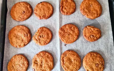Tolv nybakade chocolate chip cookies ligger på ett bakplåtspapper. De är gyllene och ser härligt sega ut.