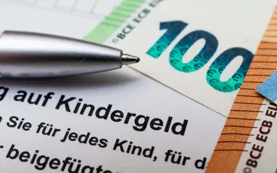 Długopis nad dokumentem o Kindergeld w Niemczech, obok banknotów 100 i 50 euro.