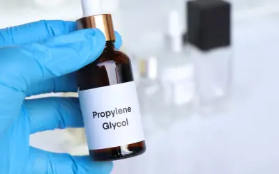 Ręka w niebieskiej rękawiczce trzyma buteleczkę z etykietą "Propylene Glycol".