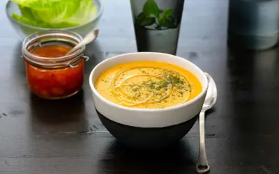 En krämig linssoppa med en virvel av olja och örter. Bredvid står en burk med en röd röra och en skål med salladsblad. Ett perfekt linssoppa recept för en mysig kväll.