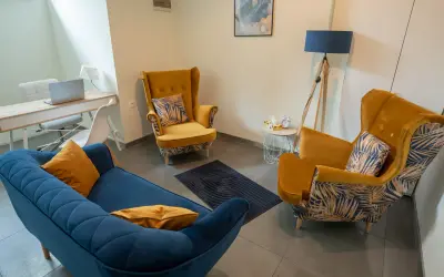 Gabinet psychologa: niebieska kanapa, dwa żółte fotele, biurko z laptopem, lampa.