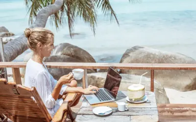Kvinna med kaffe och laptop på en strandterrass, drömmen om ett digitalt nomad jobb.