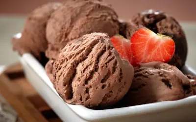 Cremoso helado de chocolate servido en un cuenco blanco, decorado con fresas frescas.