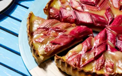 Une tranche de tarte à la rhubarbe, garnie de fruits rouges et d'une crème dorée, repose sur une assiette bleue.