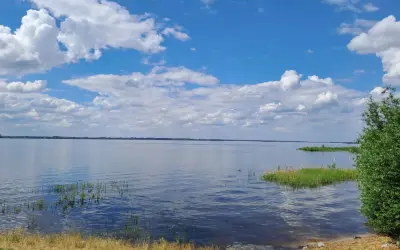 Spokojny zalew Jeziorsko w letni dzień. Błękitne niebo z białymi chmurami odbija się w tafli wody.