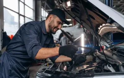 Uśmiechnięty mechanik w warsztacie sprawdza silnik. Zastanawiasz się, ile zarabia mechanik?