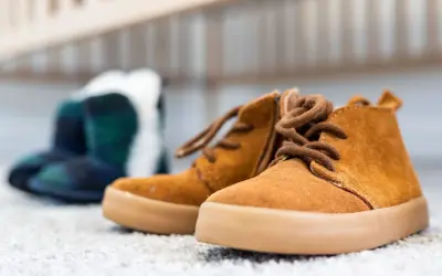 Brązowe, sznurowane buty dziecięce na pierwszym planie, w tle niebiesko-zielone botki w kratę.