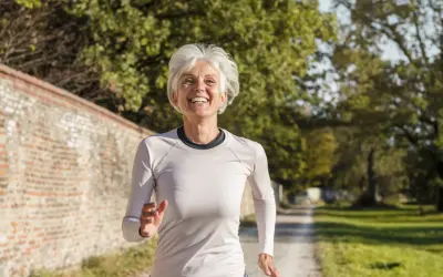 Femme souriante de 60 ans courant sur un chemin, suivant un plan d'entraînement course à pied.