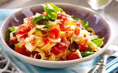 Nudeln mit Tomaten, Mozzarella, Basilikum und Speck in einer Schüssel.