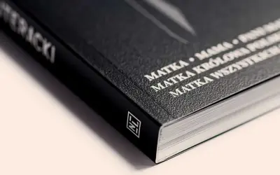 Czarny grzbiet książki z białym napisem "MATKA KRÓLOWA WSZYSTKICH SZCZĘŚLIWYCH". Ten artykuł to prawdziwe dzieło sztuki.