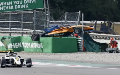 Wypadek bolidu F1 na torze Monza. Pomarańczowo-niebieski bolid leży na bandzie, ratownicy udzielają pomocy.