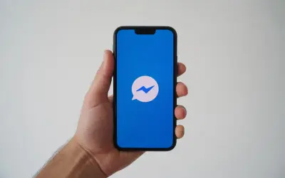 Dłoń trzyma smartfon z niebieskim ekranem i ikoną Messengera. Zastanawiasz się, dlaczego nie widzę aktywności na Messengerze?