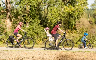 Rodzina na rowerach cieszy się aktywnym wypoczynkiem. Mama z bagażem, tata z córką w foteliku i mały chłopiec na swoim rowerze – idealny przykład turystyki rowerowej.