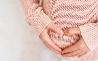 Dłonie tworzą serce na brzuchu ciężarnej. Warto pamiętać, że żółte upławy w ciąży mogą być sygnałem do konsultacji z lekarzem.