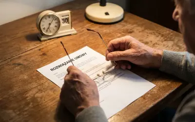 Starszy mężczyzna z okularami w dłoniach czyta dokument "Rozwiązanie umowy". Czy można zwolnić emeryta? Zegar pokazuje 30. dzień miesiąca.