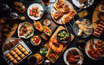 Bogactwo tapas: krewetki, pieczywo z dodatkami, ser, wędliny i inne przysmaki na czarnym stole.