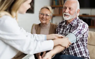 Un médecin vérifie la tension d'un homme âgé, 15/8 de tension, tandis que sa femme souriante observe.
