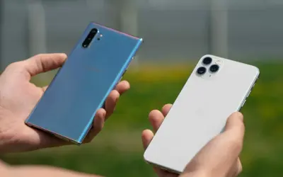 Dwie dłonie trzymają telefony: niebieski Samsung i biały iPhone. Który wybierasz?