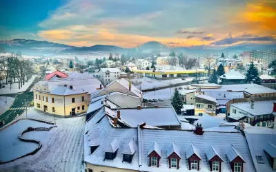 Zimowy krajobraz miasta w Czechach blisko granicy. Śnieg pokrywa dachy i ulice, a w oddali widać wzgórza.