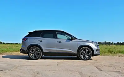 Srebrny Renault Austral z czarnym dachem stoi na polnej drodze, w tle zielone pole i błękitne niebo.