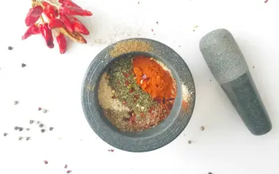 Mortier en pierre rempli d'épices pour fajitas, avec des piments rouges séchés et des grains de poivre à proximité.