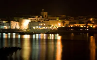Otranto di notte: luci, castello e riflessi sull'acqua. La città si anima, pronta per le discoteche estive.