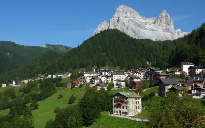 Villaggio alpino con case in pietra e legno, circondato da boschi e verdi pascoli, sotto un'imponente cima rocciosa. Il rifugio Venezia è un luogo incantevole.