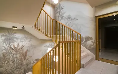 Habillage mur cage d'escalier avec un décor tropical en camaïeu. Escalier en marbre et rambarde en bois doré.