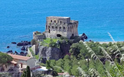 Torre aragonese a picco sul mare, uno dei borghi da visitare in Calabria, con case e vegetazione lussureggiante.