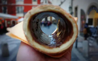 Trdelník z czekoladą, jeden z pysznych czeskich przysmaków, widziany przez jego wnętrze na tle ulicy.