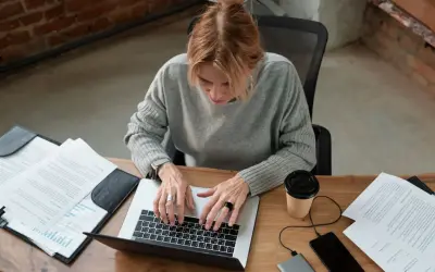 Kobieta pracuje przy laptopie, analizując dokumenty. Zastanawia się, czy umowa zlecenie wlicza się do stażu pracy, szukając odpowiedzi online.