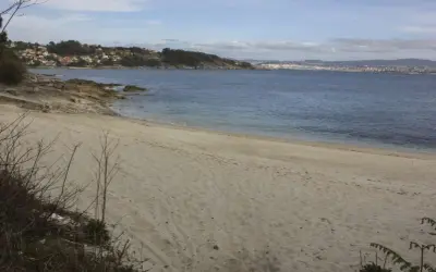 Arena dorada en la playa temperans, con el mar azul y una ciudad al fondo.