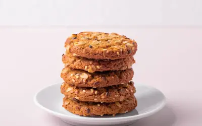 Ein Stapel knuspriger Kekse ohne Zucker, verfeinert mit Haferflocken und Samen, auf einem weißen Teller.