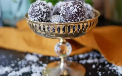 Nyttiga chokladbollar rullade i kokosflingor, serverade i en vacker guldfärgad skål. En perfekt, hälsosam godsak!