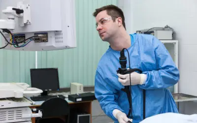 Lekarz w niebieskim fartuchu i okularach ochronnych trzyma endoskop, przygotowując się do badania. Czy gastroskopia boli? Procedura jest zazwyczaj bezbolesna.