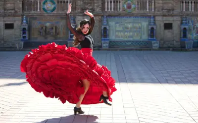Kobieta w czerwonej, falbaniastej sukni wykonuje pełen pasji flamenco taniec na tle zabytkowej budowli.