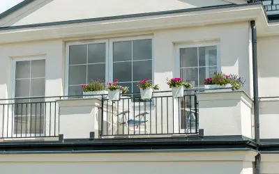 Białe okna pięknie komponują się z jasną, kremową elewacją budynku. Balkon ozdobiony kwiatami dodaje uroku.