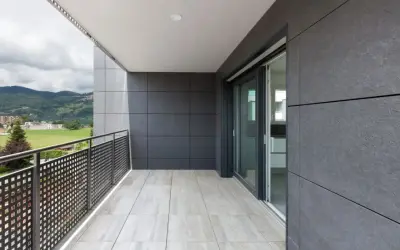 Nowoczesny balkon z jasnymi płytkami na podłodze i ciemnymi panelami na ścianie. To właśnie gres, trwały i estetyczny materiał, idealny na zewnątrz.