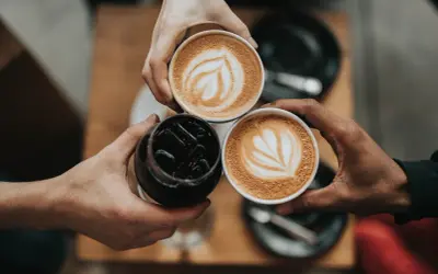 Tre händer håller varsin kopp med kaffe. Två koppar har vacker latte art, en är en kaffe macchiato.