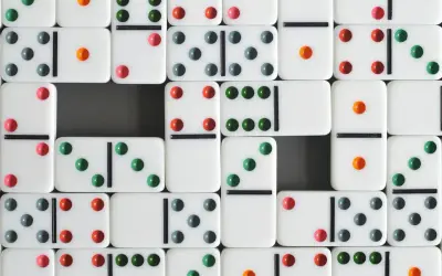 Wiele białych kostek do gry w domino z kolorowymi kropkami (zielonymi, czerwonymi, szarymi i pomarańczowymi) ułożonych w rzędy.