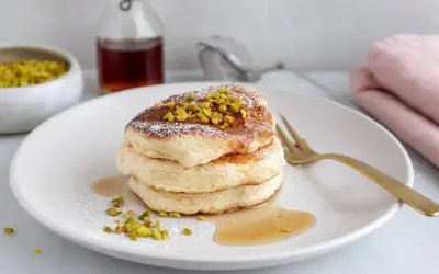 Fluffiga japanska pannkakor toppade med pistagenötter och pudersocker, serverade med sirap.