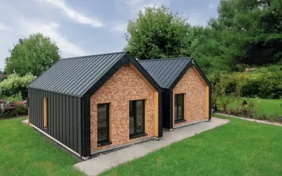 Nowoczesny dom drewniany z ceglanymi akcentami i grafitowym dachem, otoczony zielenią.