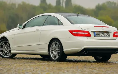 Biały w212 coupe z polskimi tablicami rejestracyjnymi stoi na mokrej nawierzchni.
