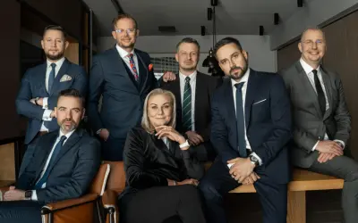 Grupa siedmiu profesjonalistów w garniturach, pozujących do zdjęcia w nowoczesnym biurze.