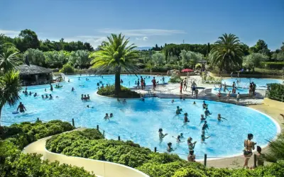 En stor pool med många badande människor, palmer och en vattenrutschkana. Perfekt för camping i Italien.