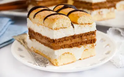 Kawałek ciasta z biszkoptem, kremem mascarpone i karmelem, ozdobiony czekoladą.